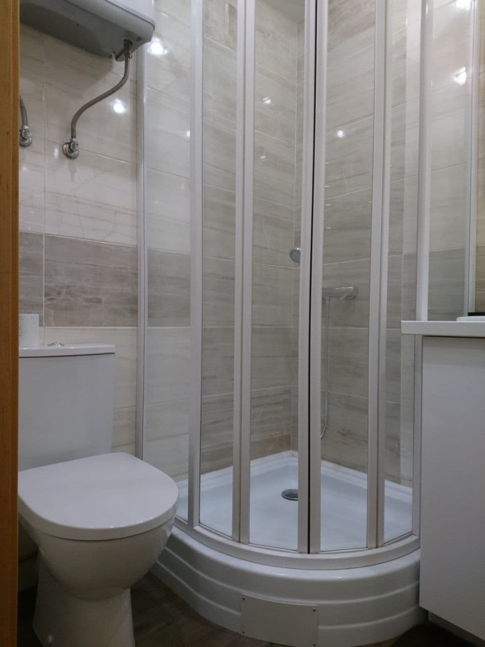 Nowoczesna kabina prysznicowa z przesuwnymi drzwiami w łazience w Legnicy, widok na toaletę i bojler na ścianie.