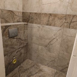 WYKOŃCZENIE WNĘTRZ DENYS POLTAVETS - Fragment łazienki z marmurowymi płytkami w odcieniach beżu i brązu, widoczny stelaż podtynkowy WC z szarym panelem przycisków, otwory instalacyjne w ścianie.