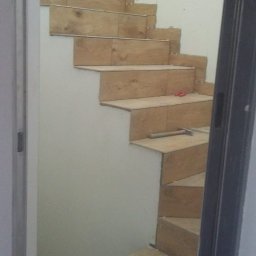 WYKOŃCZENIE WNĘTRZ DENYS POLTAVETS - Montaż płytek imitujących drewno na schodach wewnętrznych, widoczne narzędzia glazurnicze i niedokończone fugowanie.