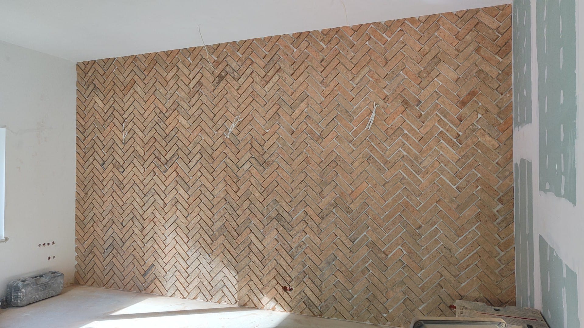 Ściana wyłożona cegiełkami w jodełkę, widoczne przewody i fragment ściany z płyt gipsowo-kartonowych przed wykończeniem.