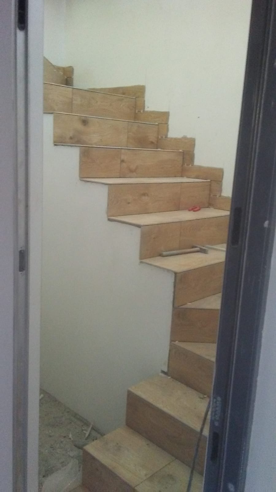 Montaż płytek imitujących drewno na schodach wewnętrznych, widoczne narzędzia glazurnicze i niedokończone fugowanie.