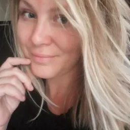 Portret uśmiechniętej blondynki z ręką pod brodą, wykonany w naturalnym świetle.