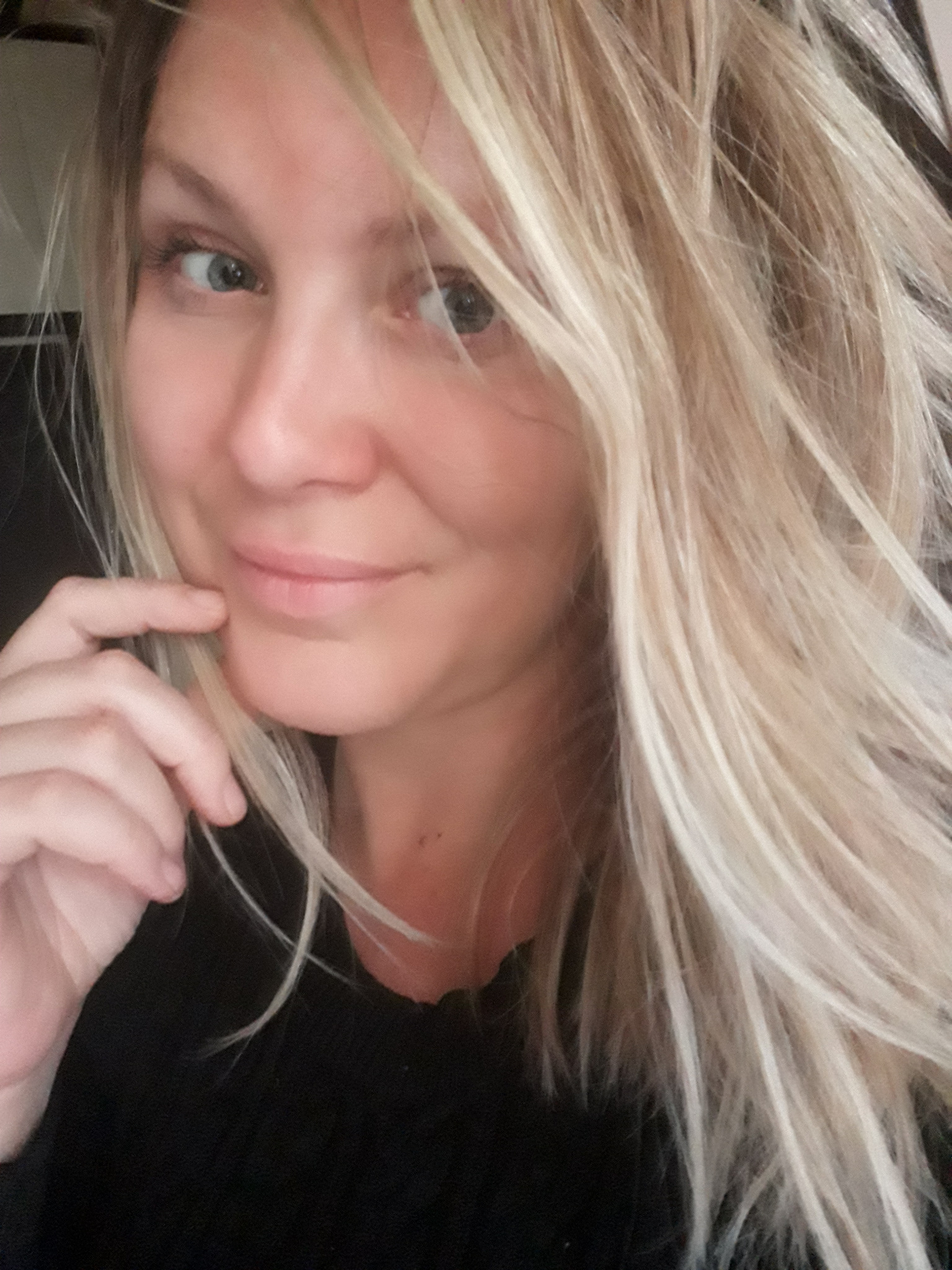 Portret uśmiechniętej blondynki z ręką pod brodą, wykonany w naturalnym świetle.