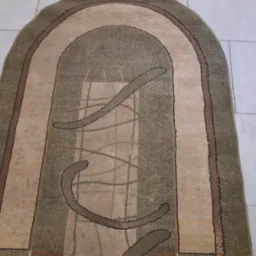 Owalny dywan w odcieniach beżu i zieleni z abstrakcyjnym wzorem na jasnych, kwadratowych płytkach podłogowych.