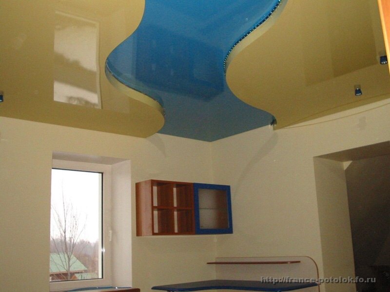 Dwupoziomowy, podwieszany sufit w kolorach beżowym i niebieskim z oświetleniem punktowym, widok na okno i meble w tle.