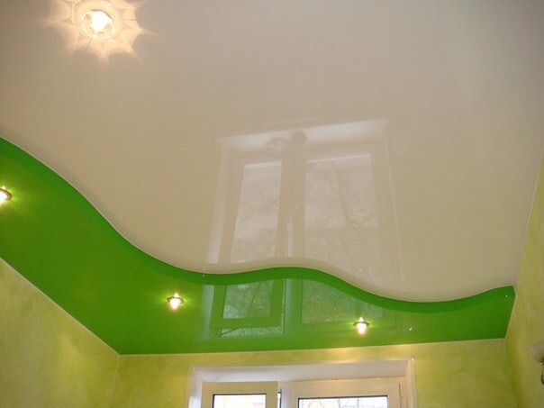 Błyszczący, biały sufit napinany z wbudowanymi punktowymi lampami, ozdobiony falującym pasem jaskrawej zieleni na styku ze ścianą, widoczne okno.