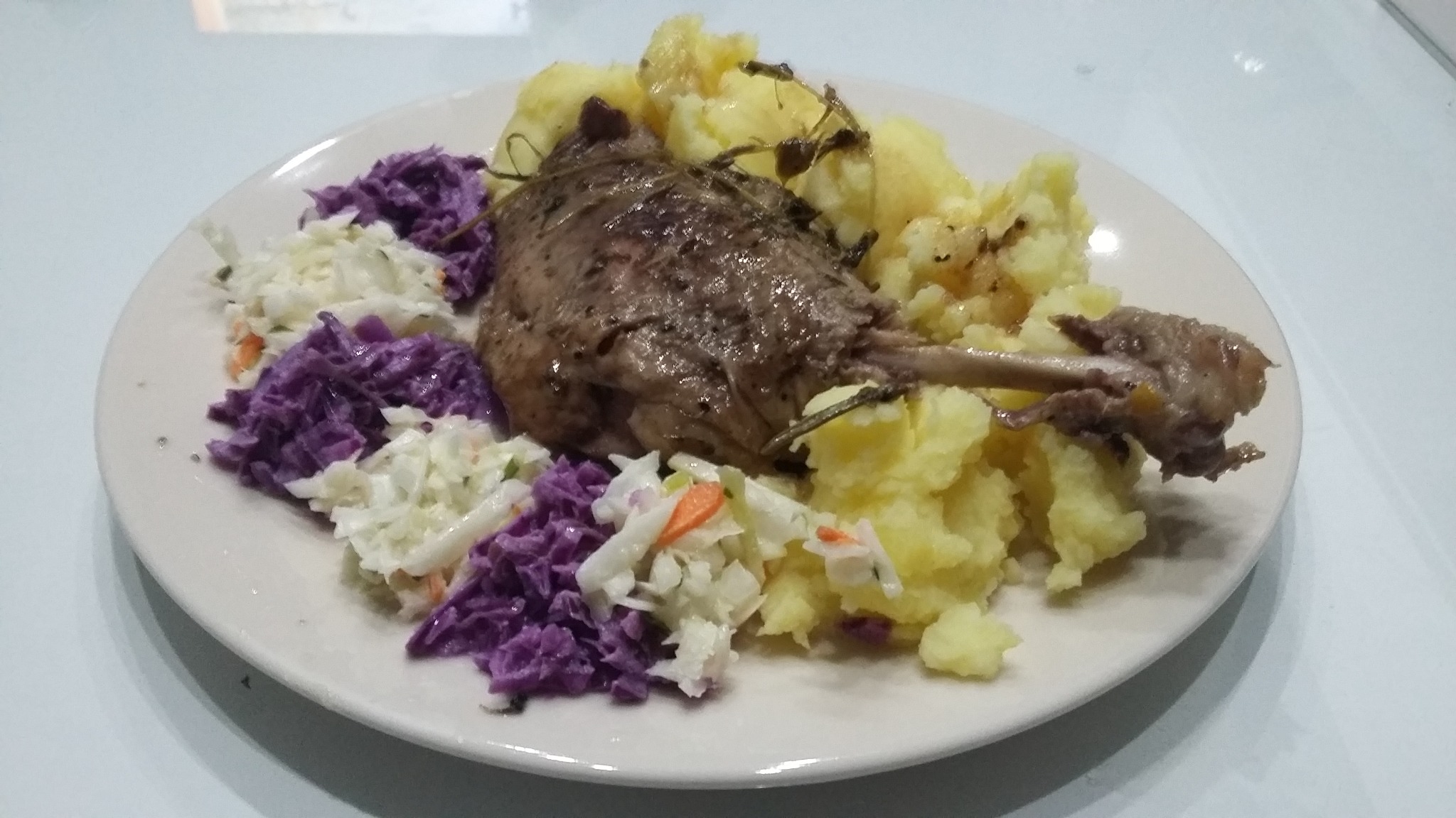 Pieczona noga z kurczaka lub kaczki z ziemniaczanym puree i surówką z białej i czerwonej kapusty na białym talerzu.