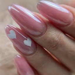 Zakochane paznokcie na Dzień Św. Walentego! Proponujemy wykonanie przedłużenia w modnym kształcie migdałów z uroczymi, walentynkowymi dodatkami. Białe serduszka, paznokcie w kolorze różowego żelu i niezastąpiony pyłek glammer.