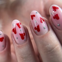 Zakochane serduszka na paznokciach! Proponujemy manicure żelowy w neutralnym odcieniu bazowym z uroczymi, walentynkowymi dodatkami - czerwonymi serduszkami i srebrnymi kropkami.