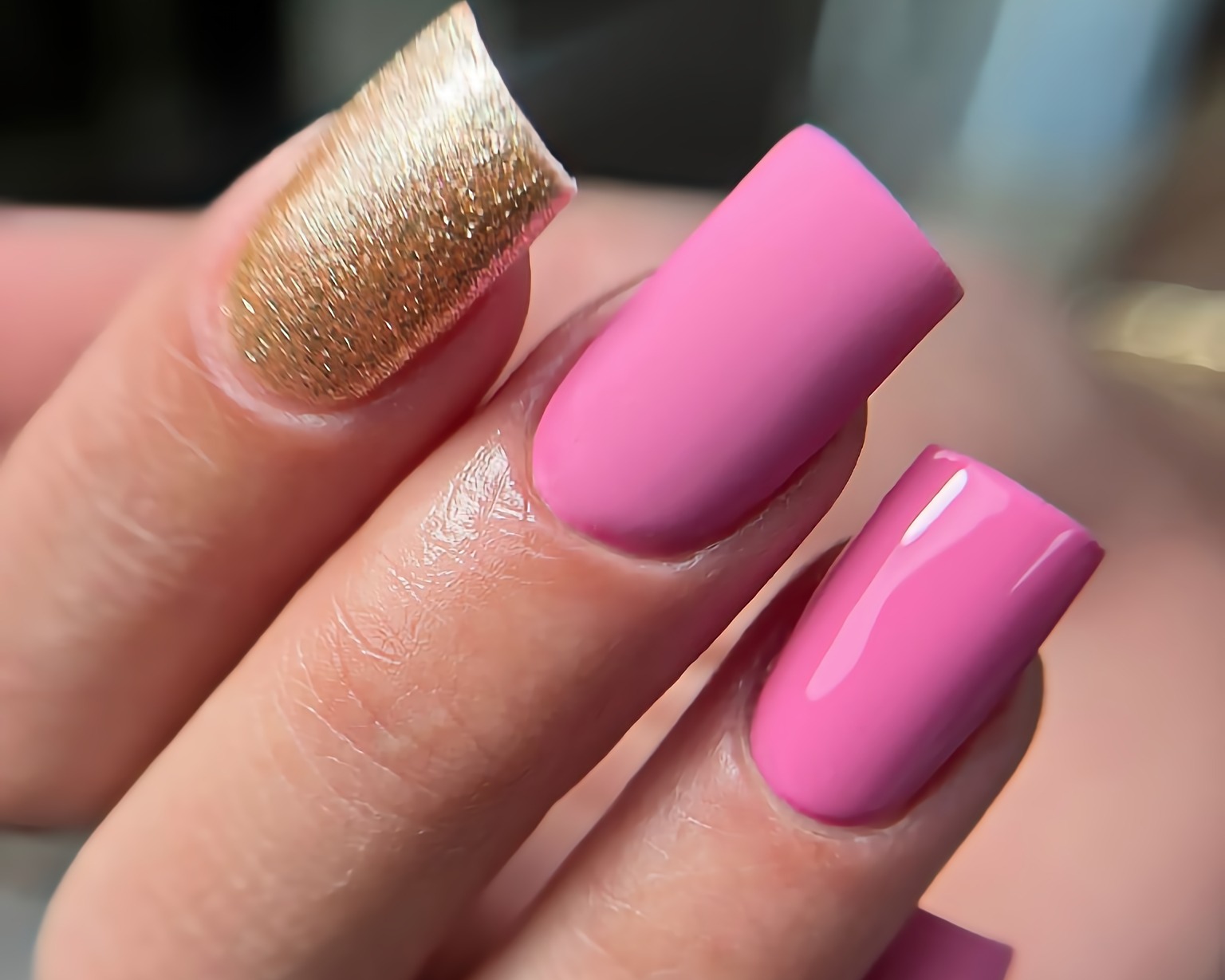 Paznokcie pomalowane na różowo i złoto, z geometrycznym kształtem, widoczne detale połyskującego złota i gładkiego różu.