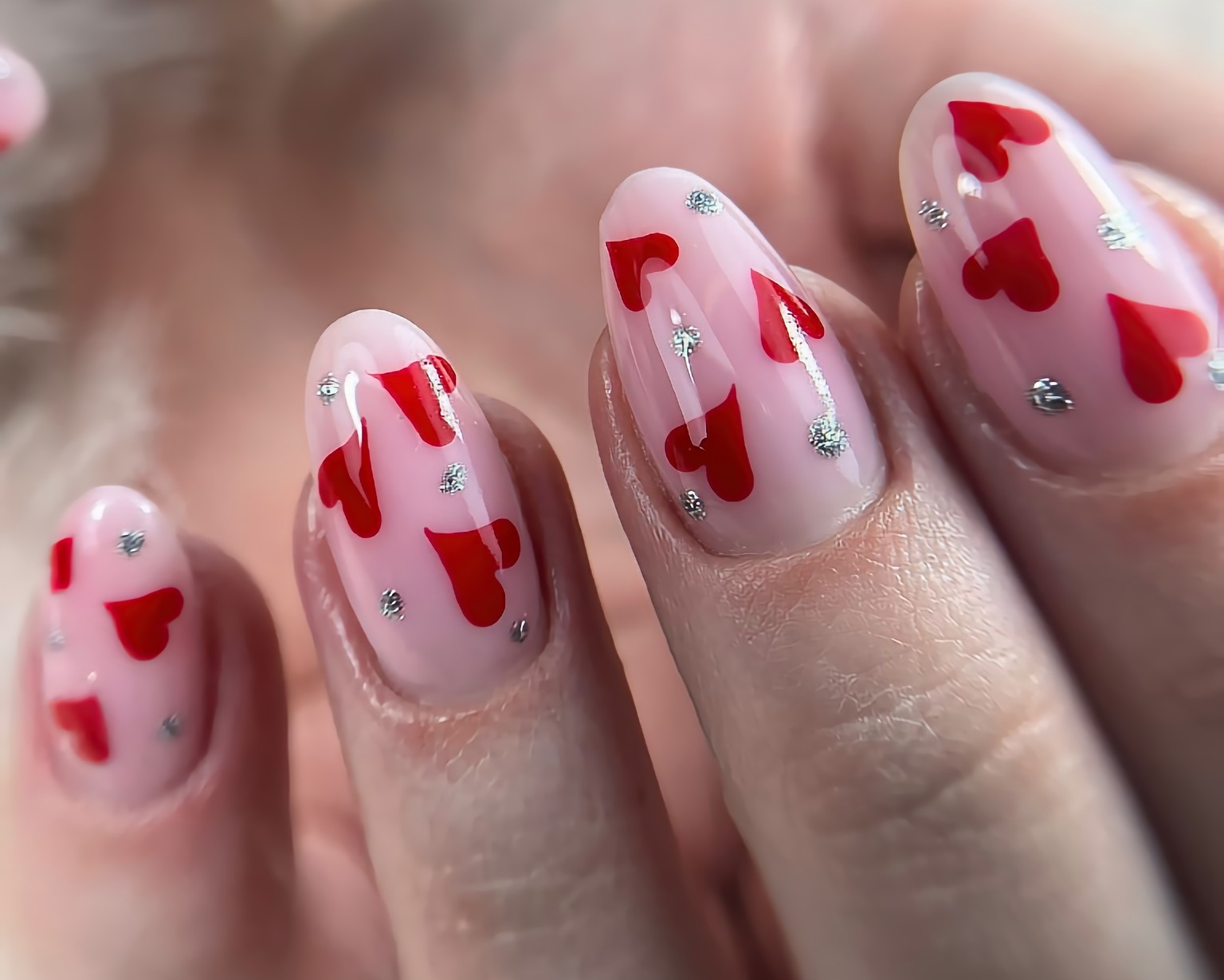 Delikatny manicure żelowy w odcieniu pudrowego różu z motywem czerwonych serduszek i srebrnych kropek, widoczne cztery paznokcie na dłoni.