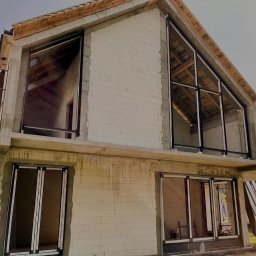 MD Construction - Surowy stan budynku z zamontowanymi oknami PCV z czarnymi ramami; widoczne rusztowanie i nieotynkowane ściany z betonu komórkowego.