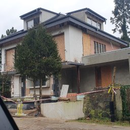 ROCKWOOD Zdzisław Gąsiorowski - Dom w trakcie remontu elewacji, okna zabite płytami, widoczne materiały budowlane i taśma ostrzegawcza.