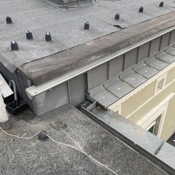 Oleksandr Kolisnyk - Płaski dach pokryty papą z zamontowanymi odpowietrznikami, widoczne metalowe orynnowanie i okno dachowe.