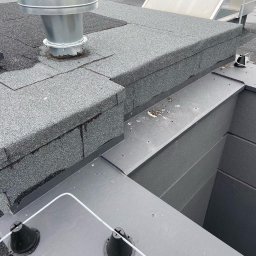 Oleksandr Kolisnyk - Płaski dach pokryty papą z kominem wentylacyjnym i zabezpieczeniami odgromowymi, widoczne detale połączeń i wykończeń.