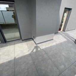 Oleksandr Kolisnyk - Szare płytki na balkonie nowoczesnego budynku, widoczny pracownik w ubraniu roboczym z butelką wody, szara elewacja budynku z oknami i drzwiami balkonowymi.