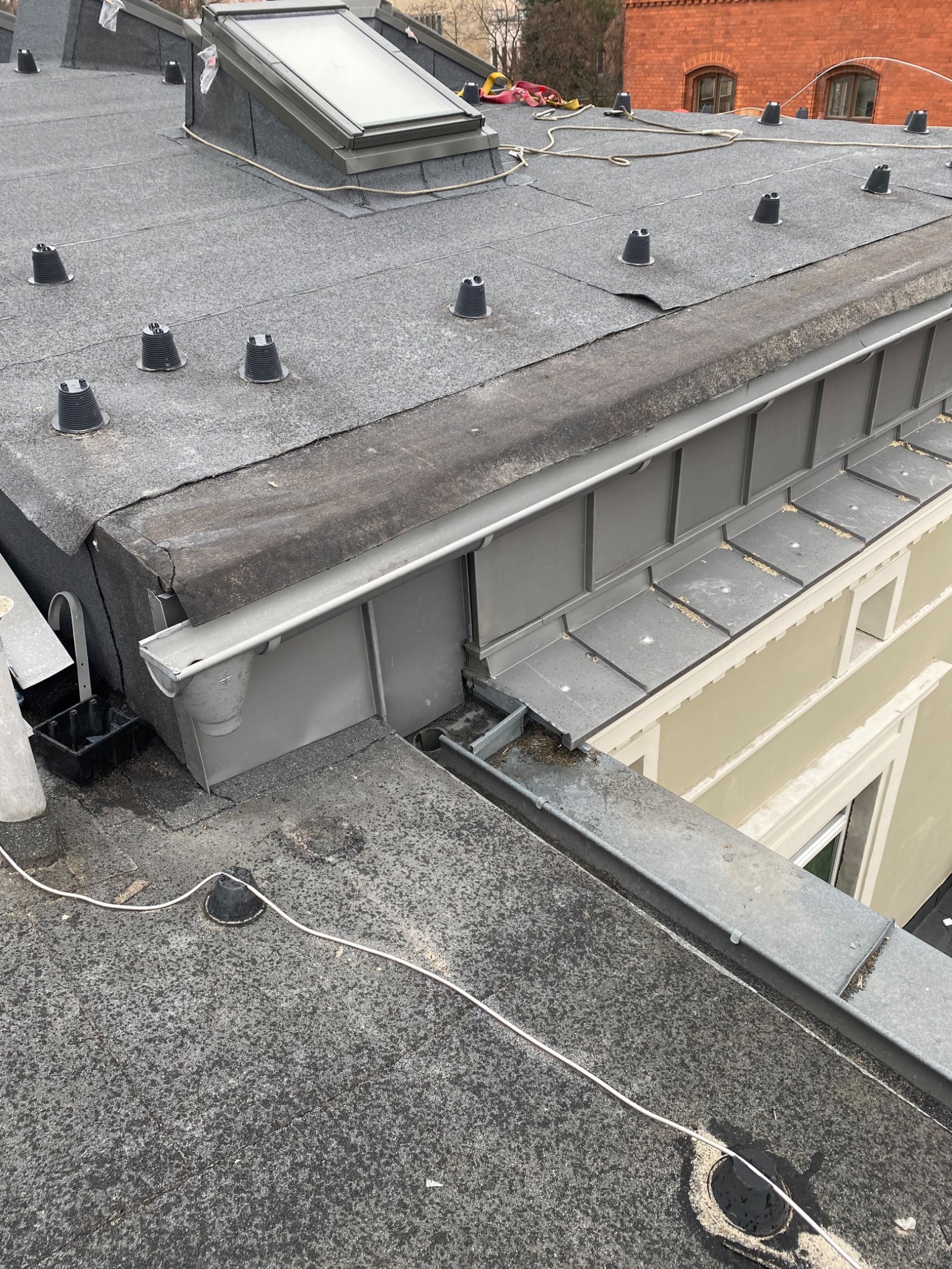 Płaski dach pokryty papą z zamontowanymi odpowietrznikami, widoczne metalowe orynnowanie i okno dachowe.