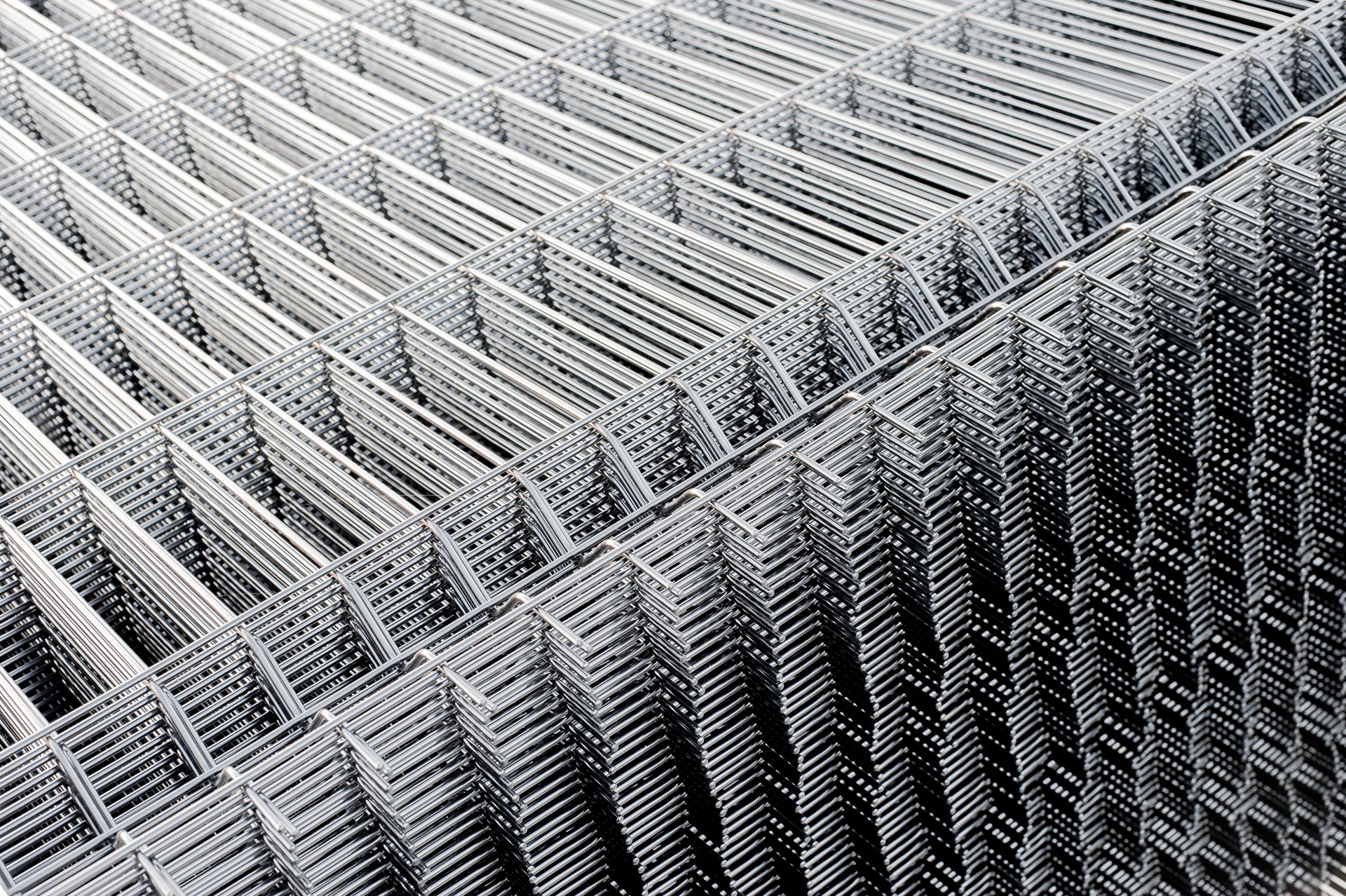Stos ocynkowanych, spawanych siatek z drutu, ułożonych pod kątem, tworzących powtarzalny wzór kraty.