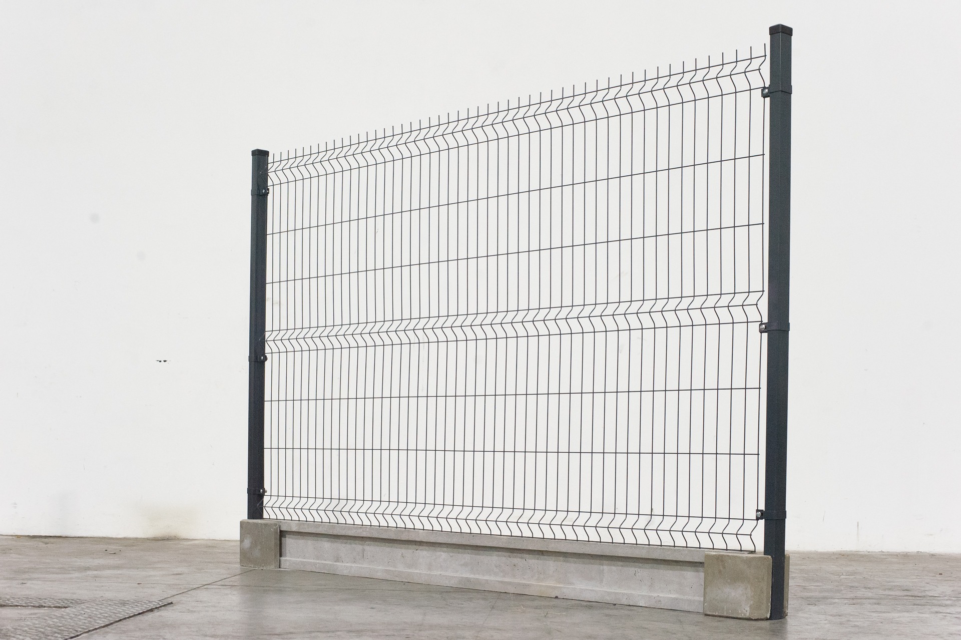 Fragment ogrodzenia z paneli zgrzewanych, mocowany do betonowej podmurówki, widoczne słupki mocujące.