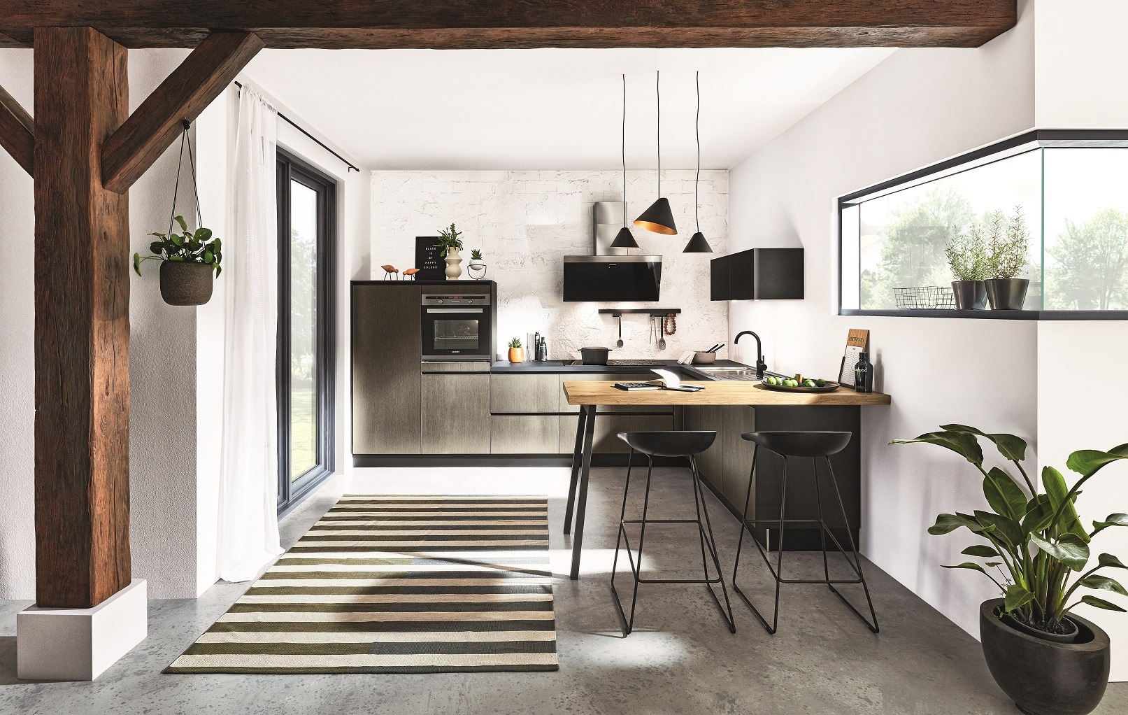 Nowoczesna kuchnia z drewnianymi belkami stropowymi, wyspą z hokerami i oknem z widokiem na zieleń. Minimalistyczny design z akcentami roślinnymi i geometrycznym dywanem.