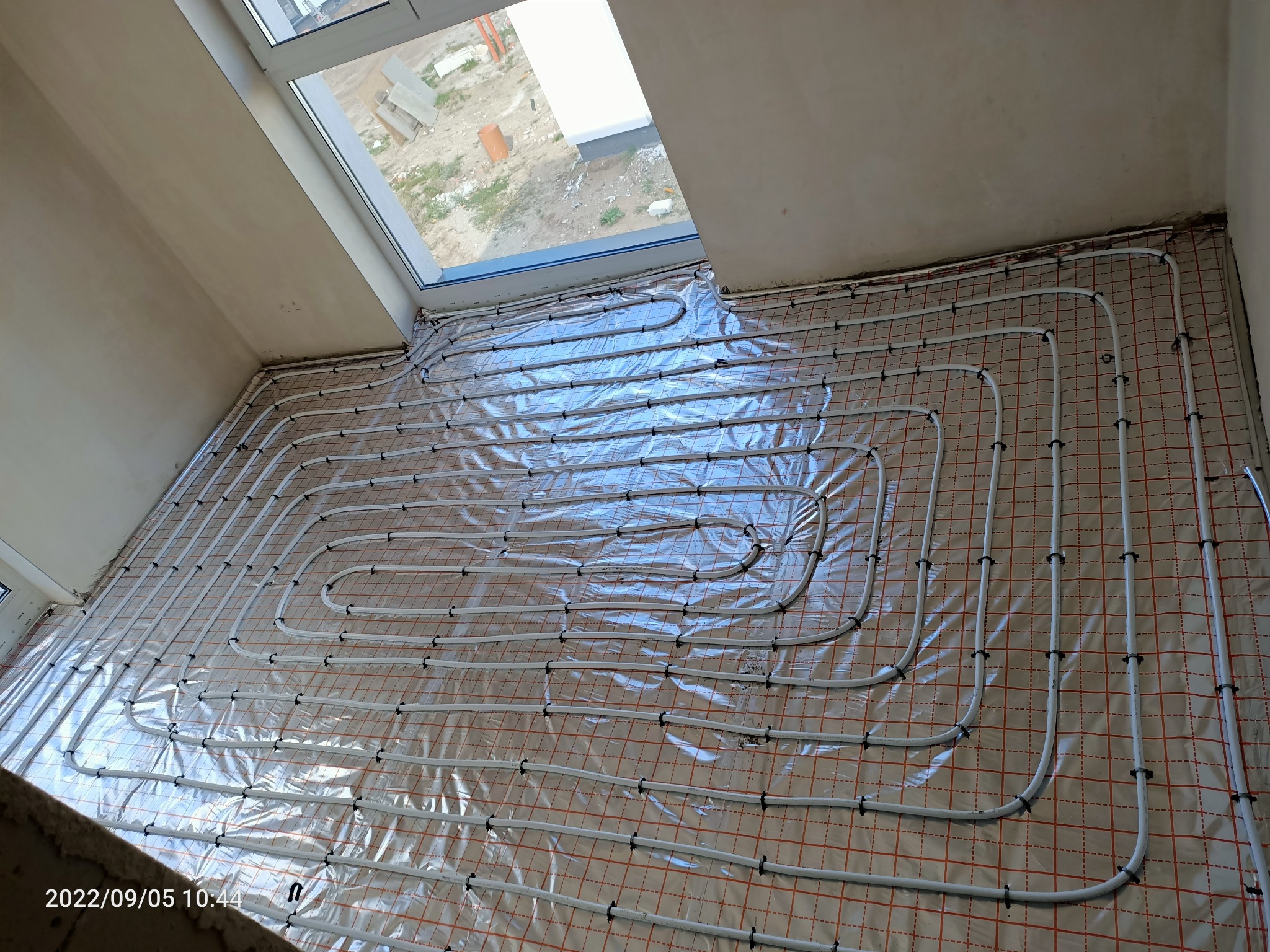 Białe rury ogrzewania podłogowego ułożone na folii z siatką w Słupsku przed wylaniem posadzki.