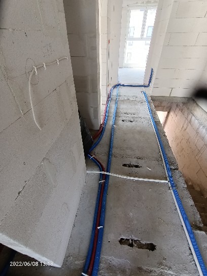 Instalacja wodna i elektryczna w surowym stanie, rury w izolacji czerwono-niebieskiej i przewody elektryczne prowadzone wzdłuż ściany z betonu komórkowego, widoczne otwory w ścianie.
