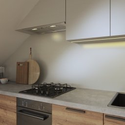 AGNIESZKA ĆWIERTNIAK-JANIA FORMAT HOME - Wizualizacja kuchni w skandynawskim stylu z drewnianymi frontami szafek, szarym blatem, czarną armaturą i płytą grzewczą, widok na skośny sufit i dekoracyjne deski do krojenia.