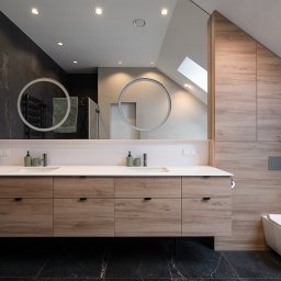 AGNIESZKA ĆWIERTNIAK-JANIA FORMAT HOME - Nowoczesna łazienka na poddaszu z drewnianą zabudową umywalki z szufladami, okrągłymi lustrami z podświetleniem LED i wiszącą toaletą.