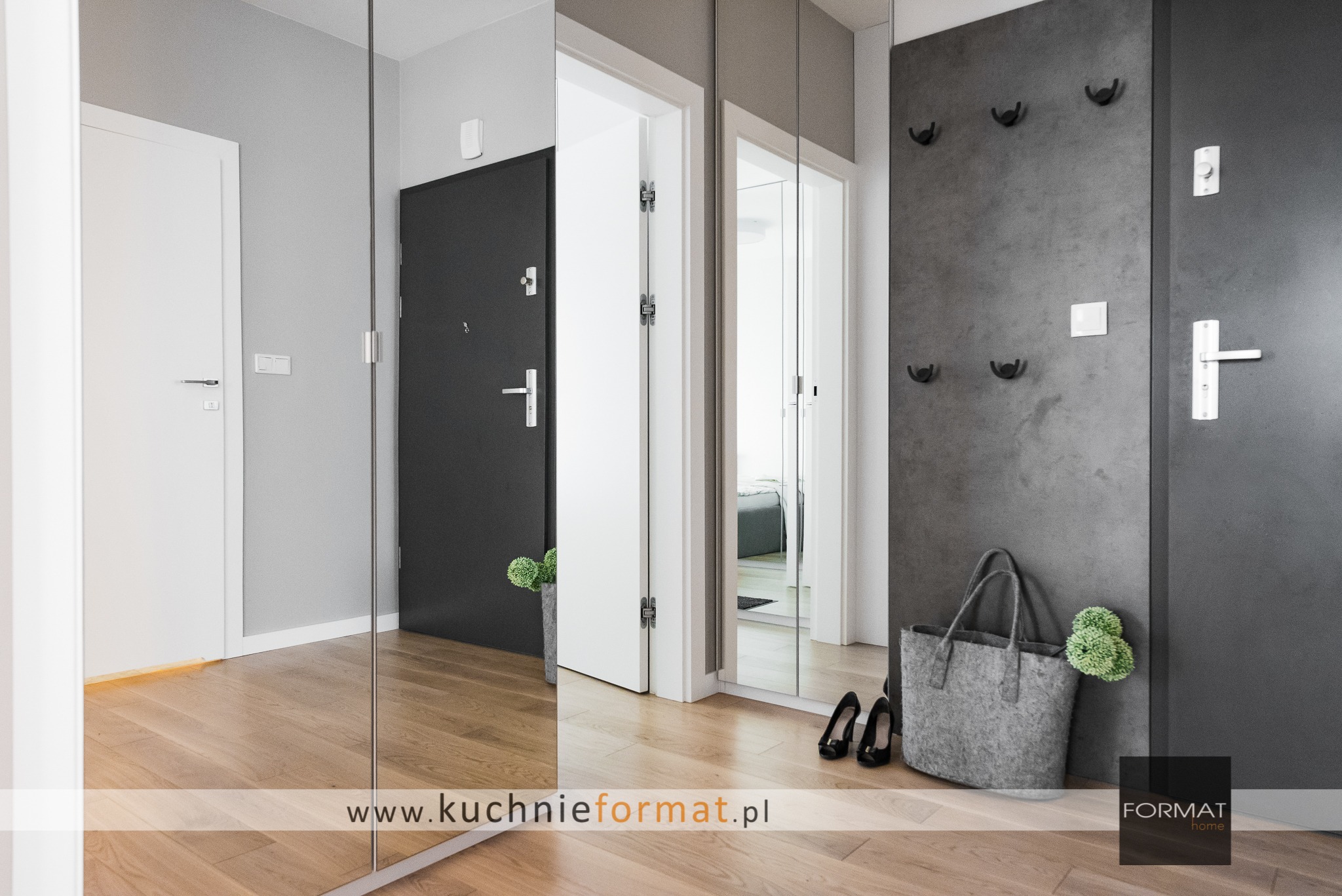 Nowoczesny przedpokój z szafą na wymiar z lustrzanymi drzwiami, drewnianą podłogą i szarą ścianą z wieszakami, widoczna torebka filcowa i czarne szpilki.