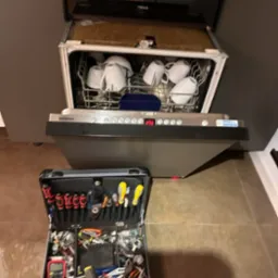 Otwarta zmywarka Siemens z naczyniami w środku, obok rozłożona walizka z narzędziami serwisowymi, widoczny wyświetlacz z kodem błędu.