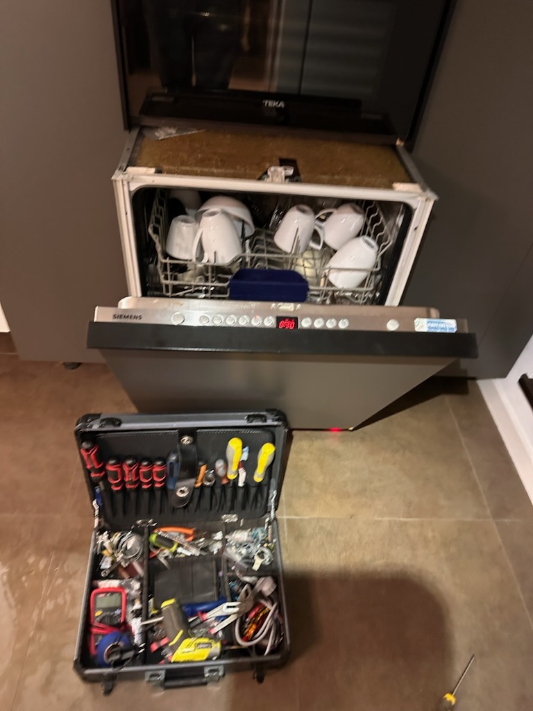 Otwarta zmywarka Siemens z naczyniami w środku, obok rozłożona walizka z narzędziami serwisowymi, widoczny wyświetlacz z kodem błędu.