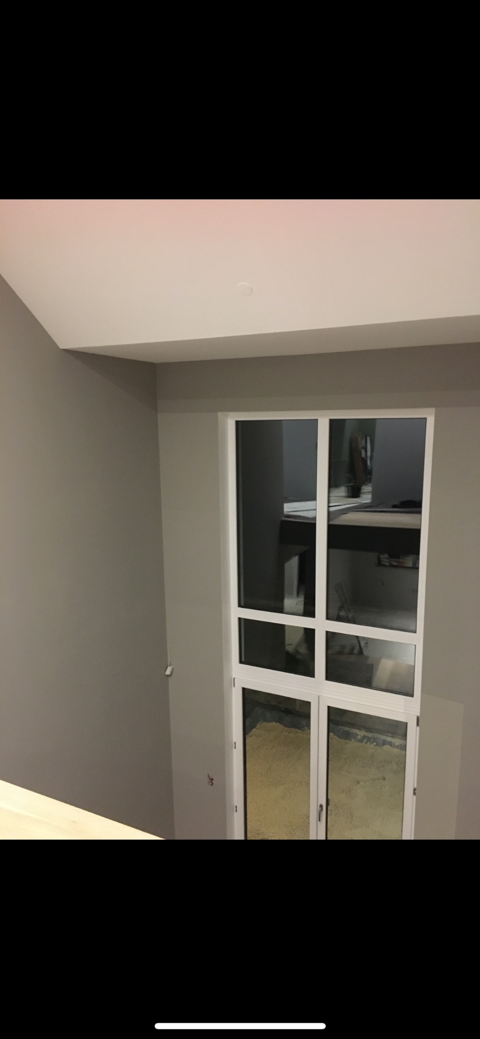 Świeżo pomalowane szare ściany w pokoju z białymi drzwiami balkonowymi, widoczne ślady po malowaniu na szybach.