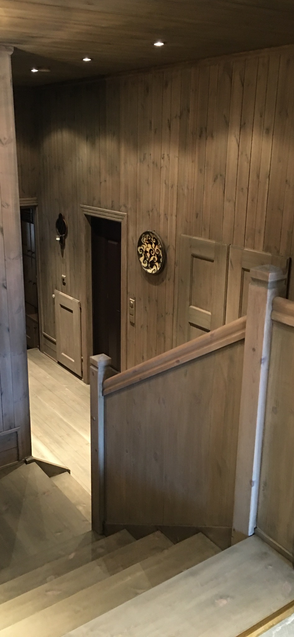 Wnętrze wykończone drewnem: widok na schody, boazerię ścienną, drzwi i dekoracyjny talerz na ścianie.