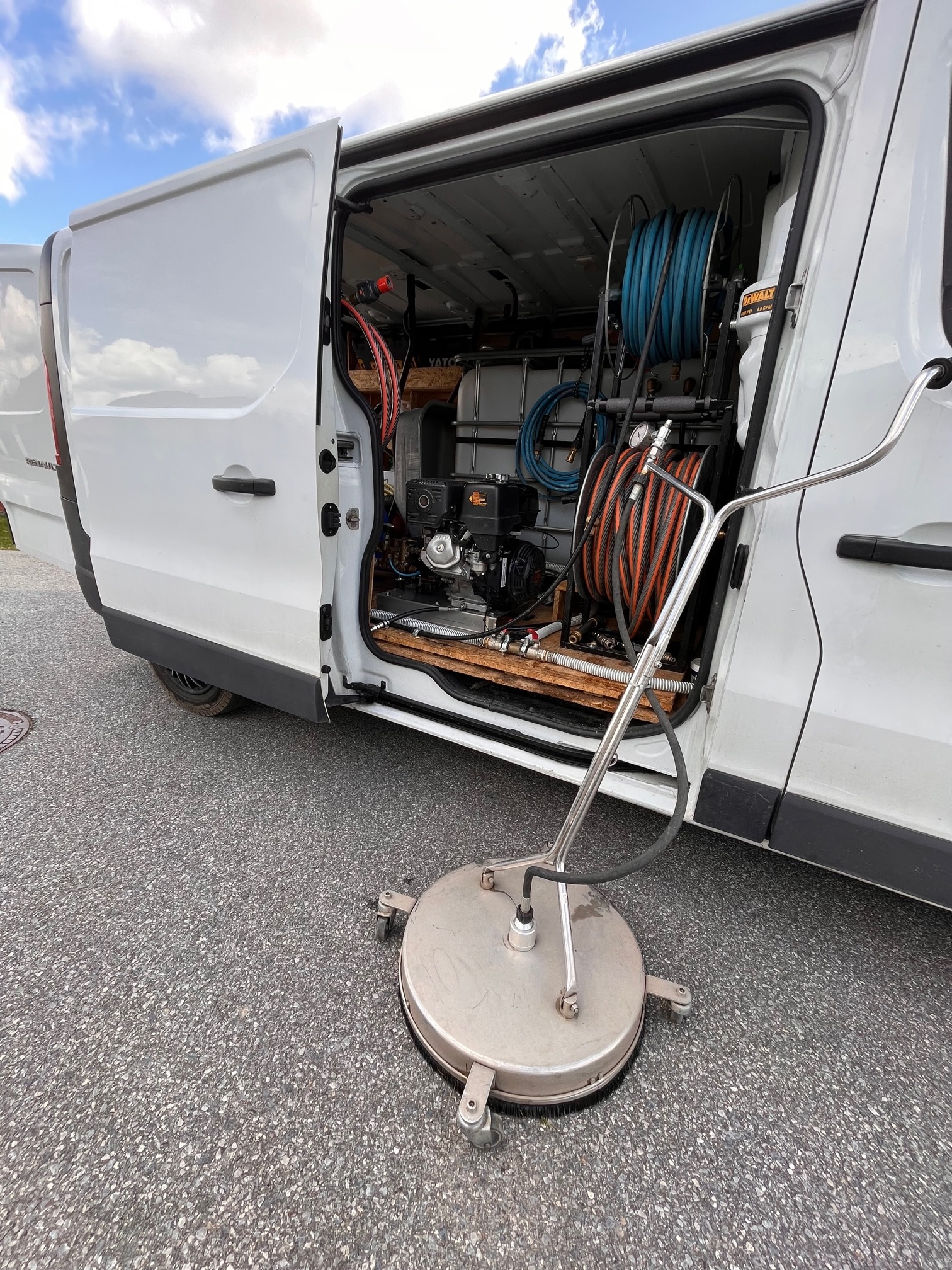 Wnętrze białego samochodu dostawczego z otwartymi drzwiami, w którym znajduje się specjalistyczny sprzęt do czyszczenia, w tym zbiornik na wodę, silnik spalinowy, zwinięte węże oraz okrągła...