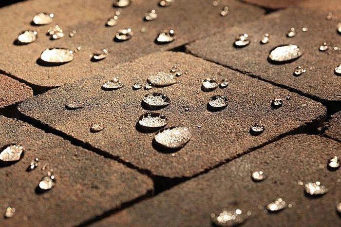 Brązowa kostka brukowa z kroplami wody po czyszczeniu, widoczne refleksy świetlne na powierzchni kropli.