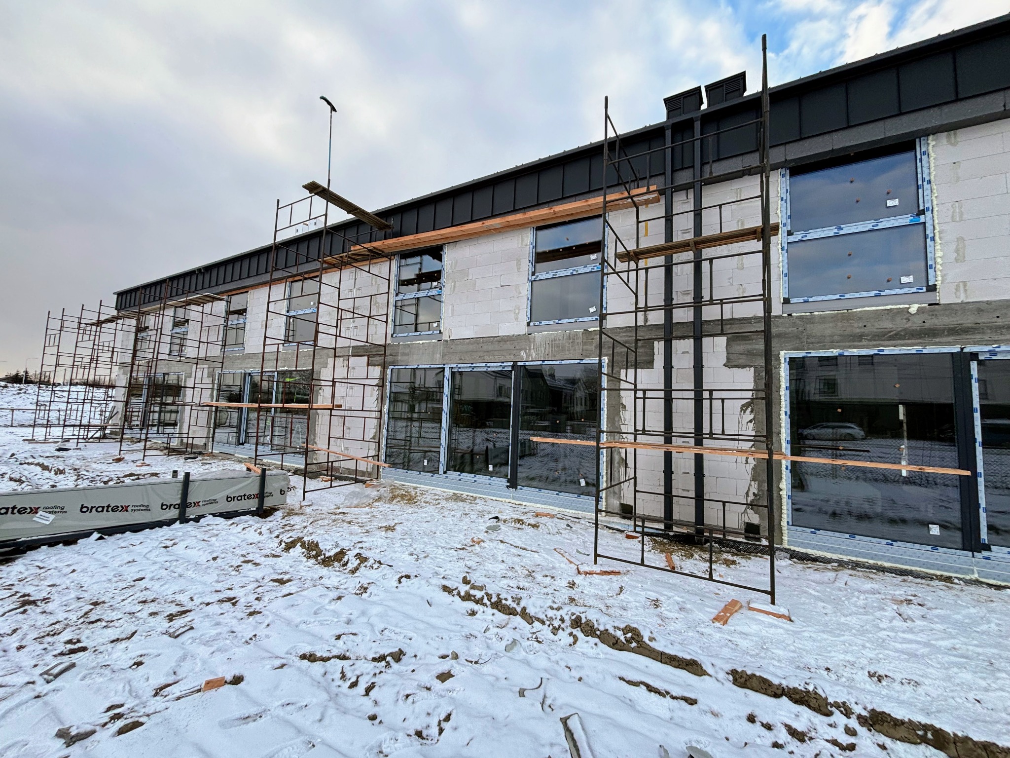Budynek w trakcie montażu okien PCV, widoczne rusztowania, ocieplenie i śnieg na ziemi.