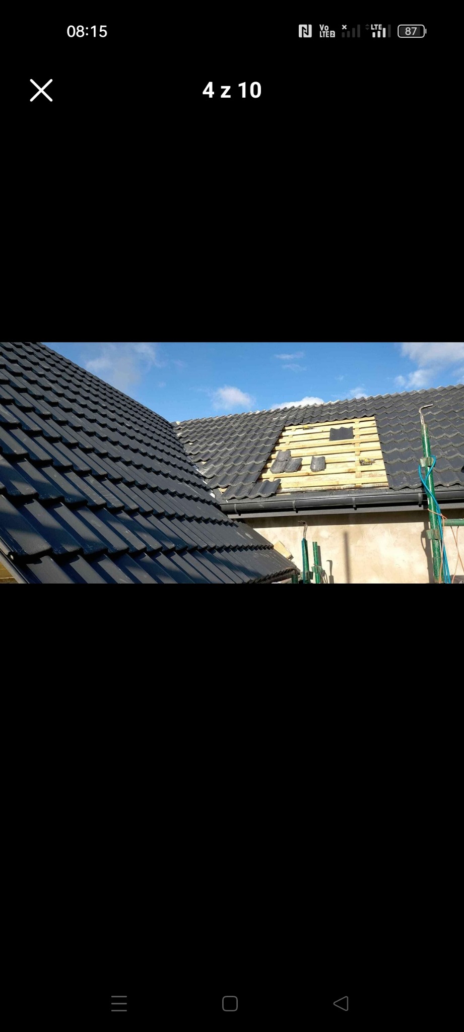 Częściowo zdjęty dach z czarnej dachówki, odsłonięta drewniana konstrukcja, fragment dachu z nową dachówką w trakcie układania, widoczne rusztowanie.