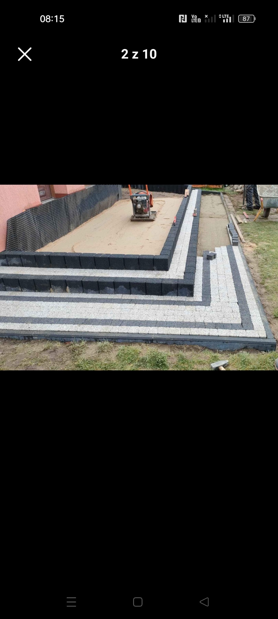 Układanie dwukolorowej kostki brukowej na schodach i ścieżce, z zagęszczarką w tle przygotowanego podłoża.