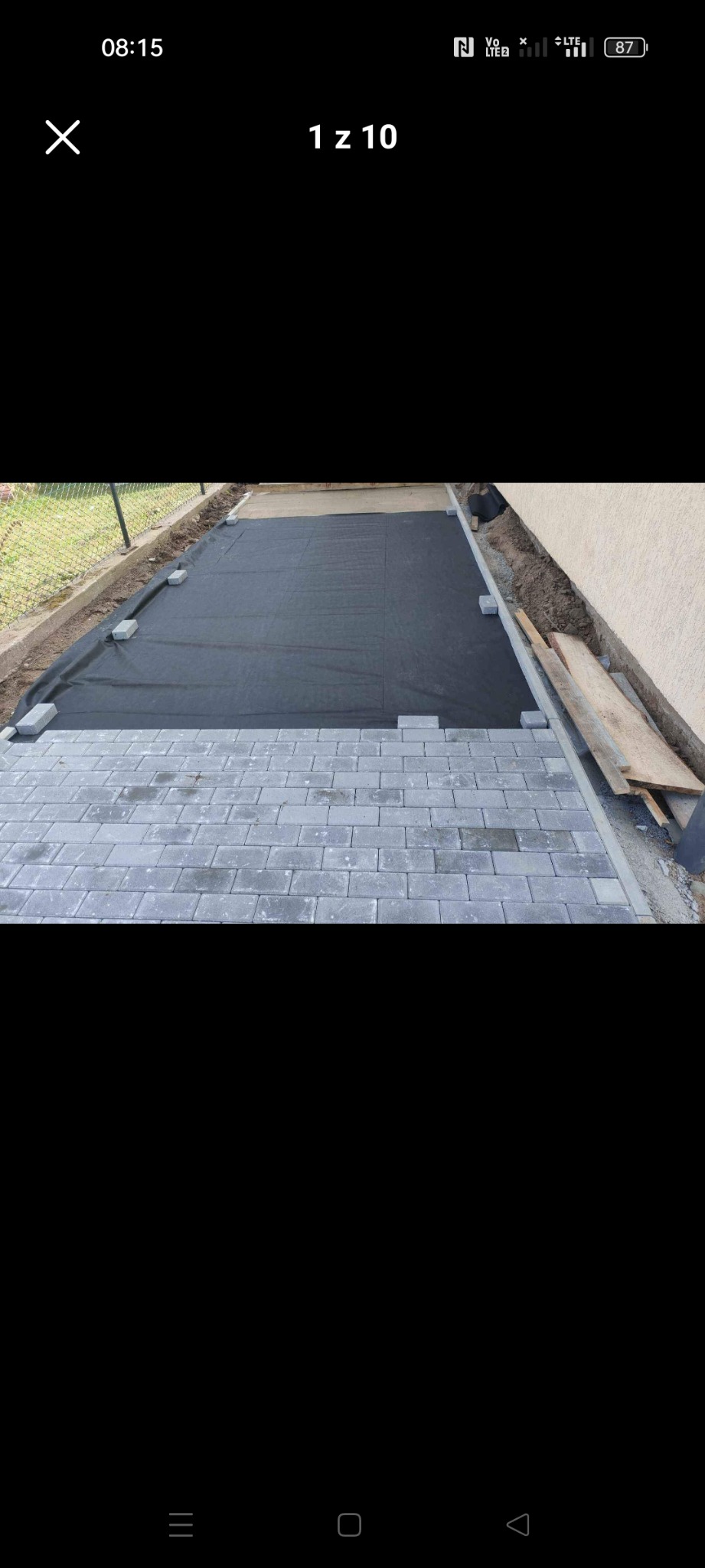 Etap przygotowania podłoża pod ścieżkę z szarej kostki brukowej: widoczna geowłóknina i częściowo ułożone obrzeża.