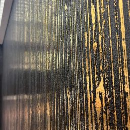 DAMIAN SYKUŁA PROBUD - Częściowy widok ściany z dekoracyjną fakturą w kolorze czarnym ze złotymi pionowymi smugami, wykonaną techniką malarską imitującą metaliczną strukturę.