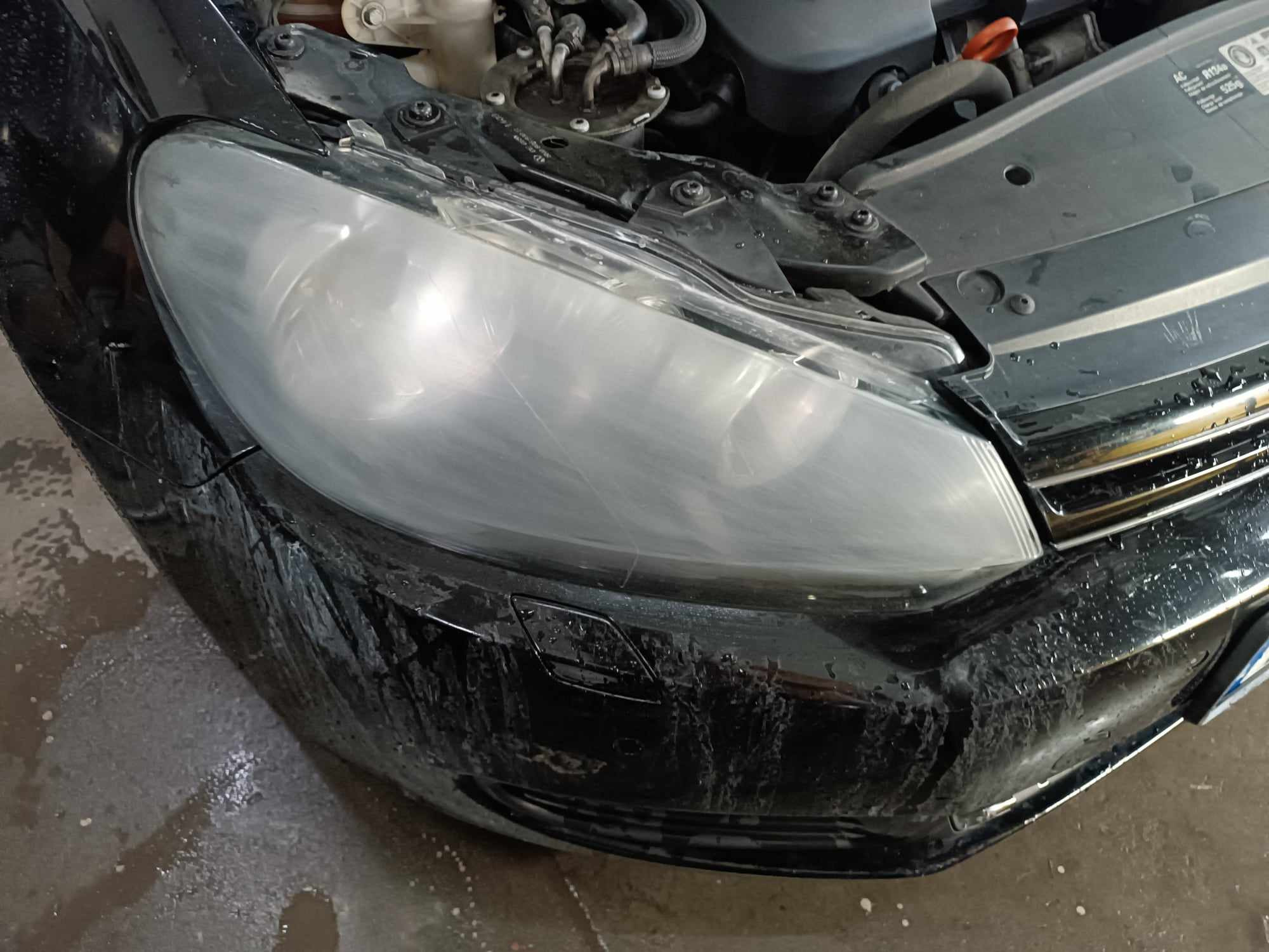 Przedni reflektor samochodu przed renowacją, widoczne zmatowienie i zarysowania na kloszu, brudny zderzak, otwarty silnik