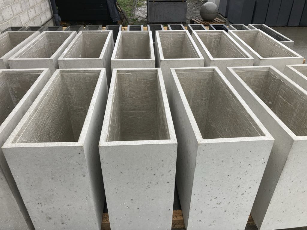 Rząd szarych, betonowych, prostokątnych donic, ustawionych na zewnątrz, z widoczną fakturą betonu i pustym wnętrzem, w tle inne elementy betonowe.