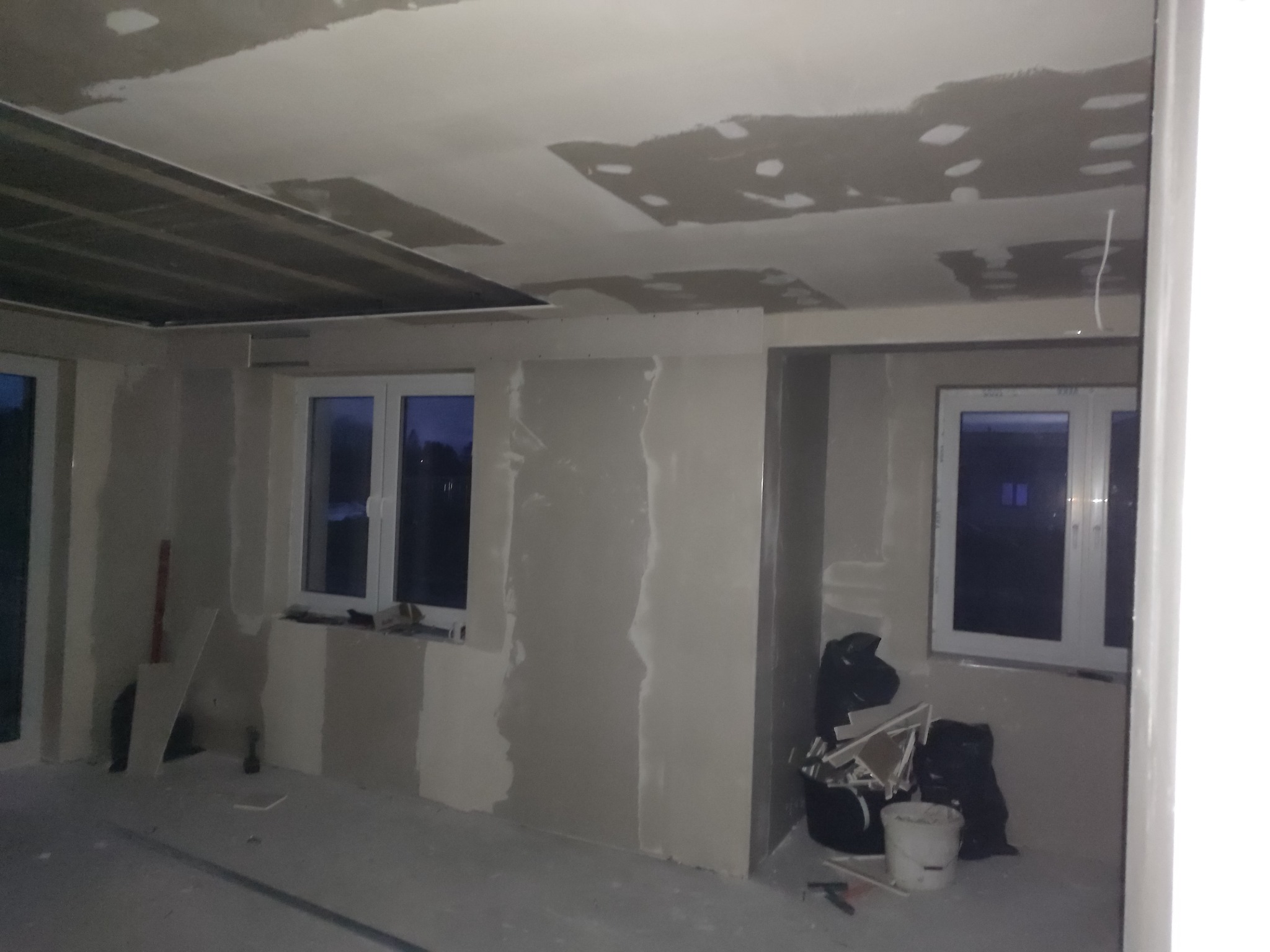 Wnętrze w trakcie remontu: widoczne ściany przygotowane do szpachlowania z widocznymi łączeniami płyt kartonowo-gipsowych, sufit z widocznymi elementami konstrukcyjnymi i śladami po szpachlowaniu...