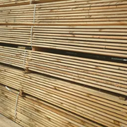 Stos tarcicy budowlanej, deski świerkowe związane taśmą, widoczne słoje drewna.