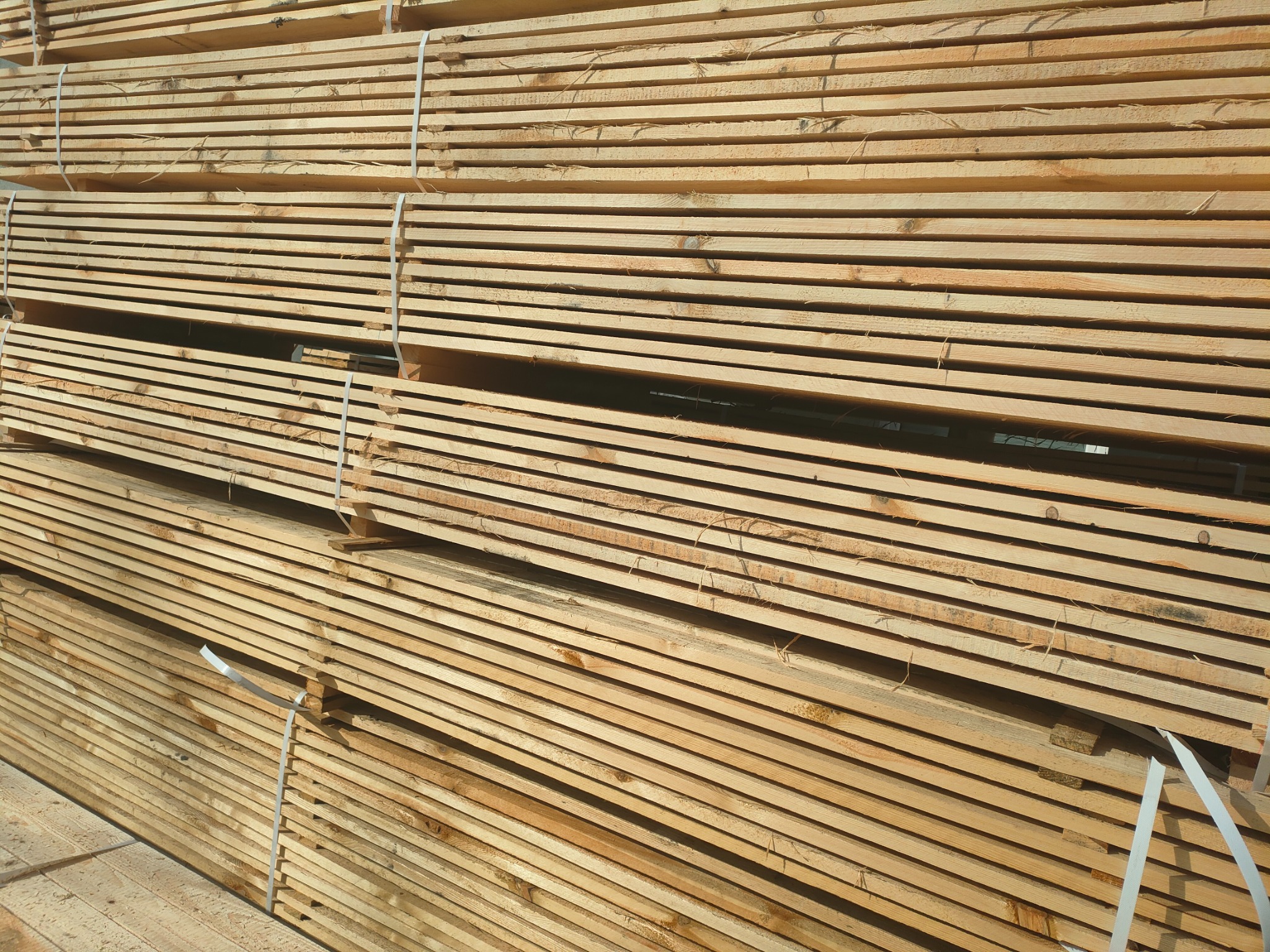 Stos tarcicy budowlanej, deski świerkowe związane taśmą, widoczne słoje drewna.