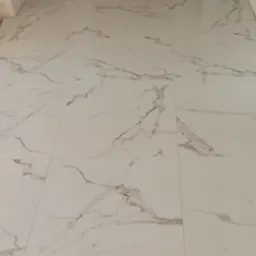 Białe płytki podłogowe z szarym marmurkowym wzorem, ułożone w regularny wzór. Widoczne fugi między płytkami.