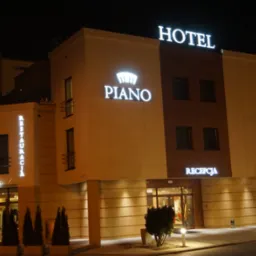Nocny widok na fasadę hotelu z podświetlonymi napisami 'HOTEL', 'PIANO' z symbolem korony i 'RESTAURACJA'.