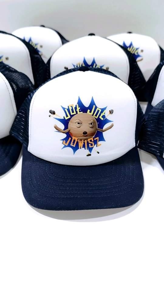 Czapka typu trucker z nadrukiem postaci z kreskówki i napisem 'JOE JOWISZ' na białym froncie, otoczona innymi czapkami z tym samym wzorem.