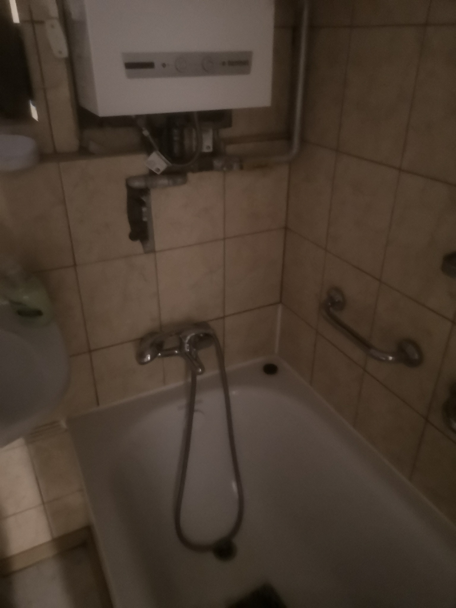 Ujęcie fragmentu łazienki z wanną, baterią, grzejnikiem gazowym i uchwytem dla niepełnosprawnych na ścianie z beżowych płytek.