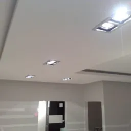 Wykończony sufit podwieszany z oświetleniem punktowym LED w nowocześnie urządzonym wnętrzu, widoczne detale wykończeniowe i gra światła.